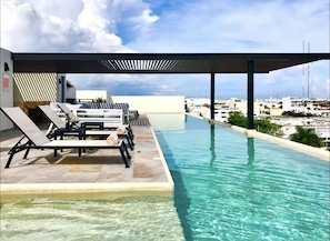 Piscina infinita no terraço, com espreguiçadeiras e vista para a paisagem urbana.