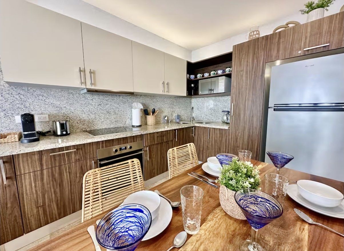 Cozinha moderna com armários de madeira, geladeira de aço inoxidável e uma mesa de jantar posta com copos e pratos.