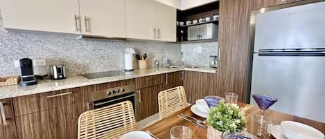A modern kitchen with wooden cabinets, a stainless steel refrigerator, and a dining table set with glassware and plates.