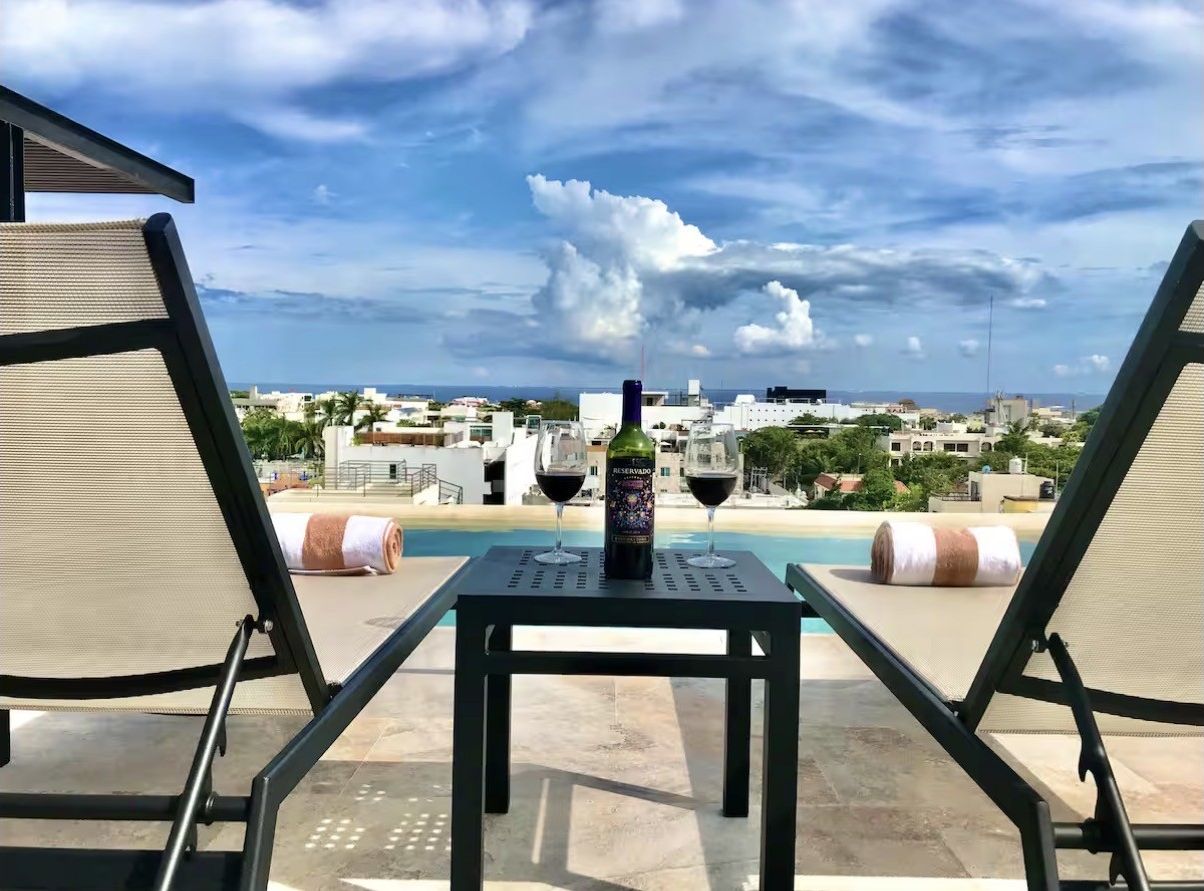 A rooftop terrace with two lounge chairs, a table, a bottle of wine, and two wine glasses.