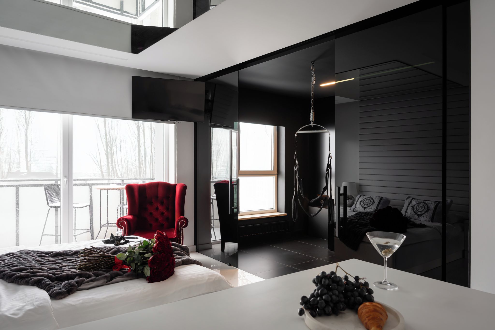 A modern interior with a bed, a red armchair, a hanging light fixture, and a martini glass on a table.