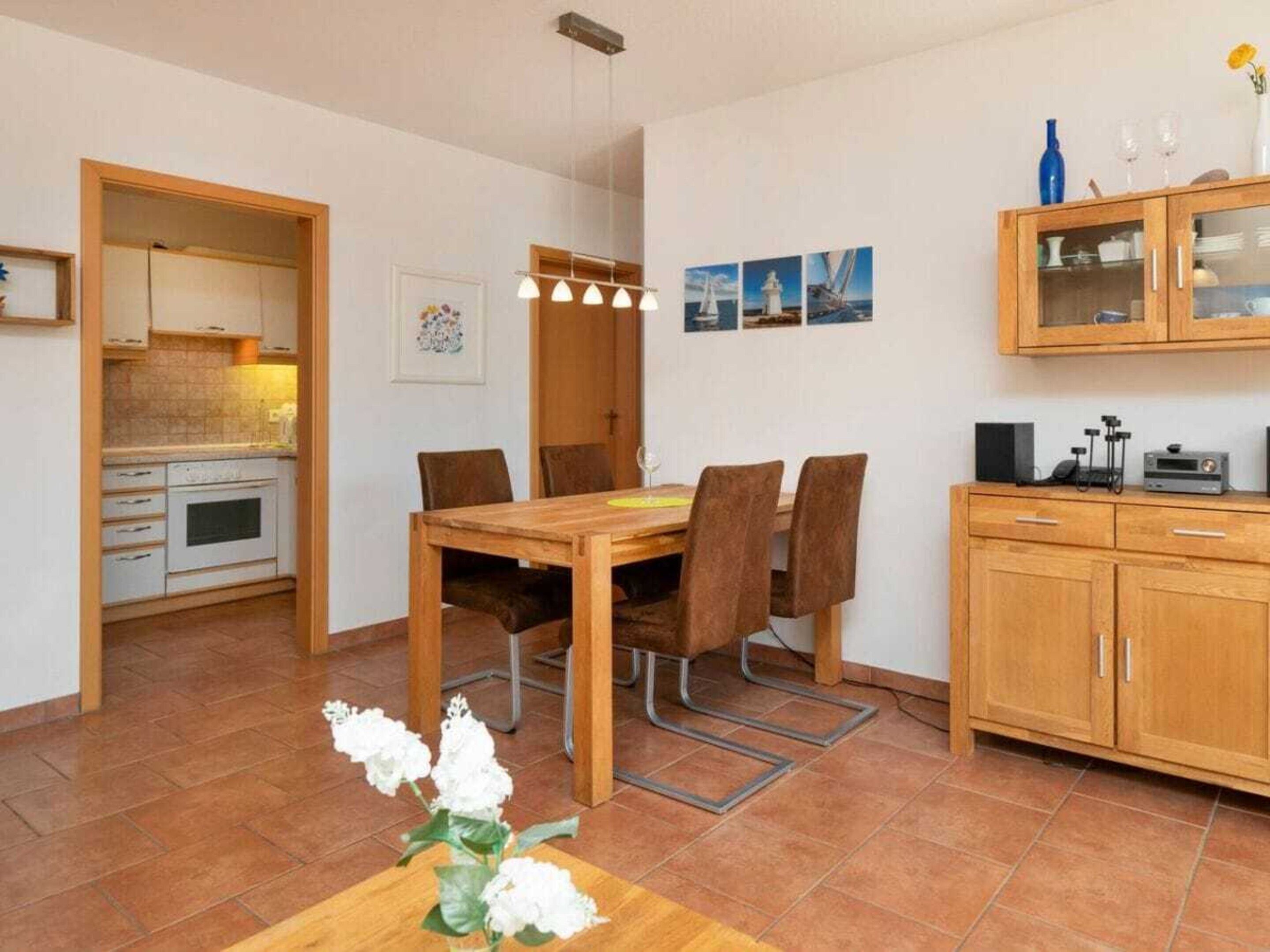 Una cocina compacta con zona de comedor, que incluye una mesa y sillas de madera, un mueble pequeño y suelo de baldosas.