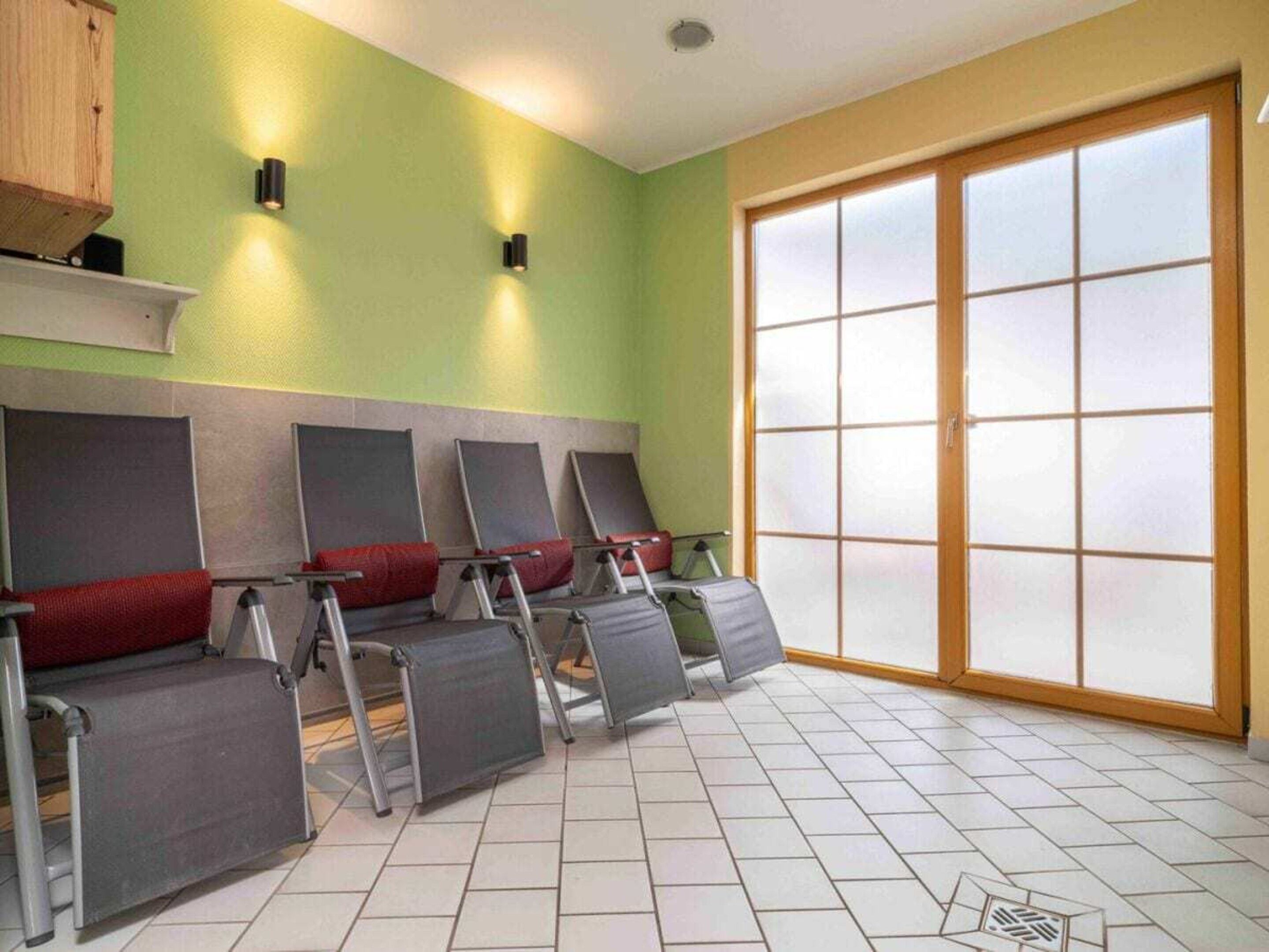 A room with a row of massage chairs, a large window, and a green wall.