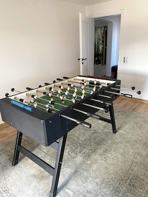 A foosball table in a room with a concrete floor and a door leading to another area. - My Time in the Harz Mountains - Your Vacation Home in the Harz Mountains. With a sauna and barbecue area. (Goslar)