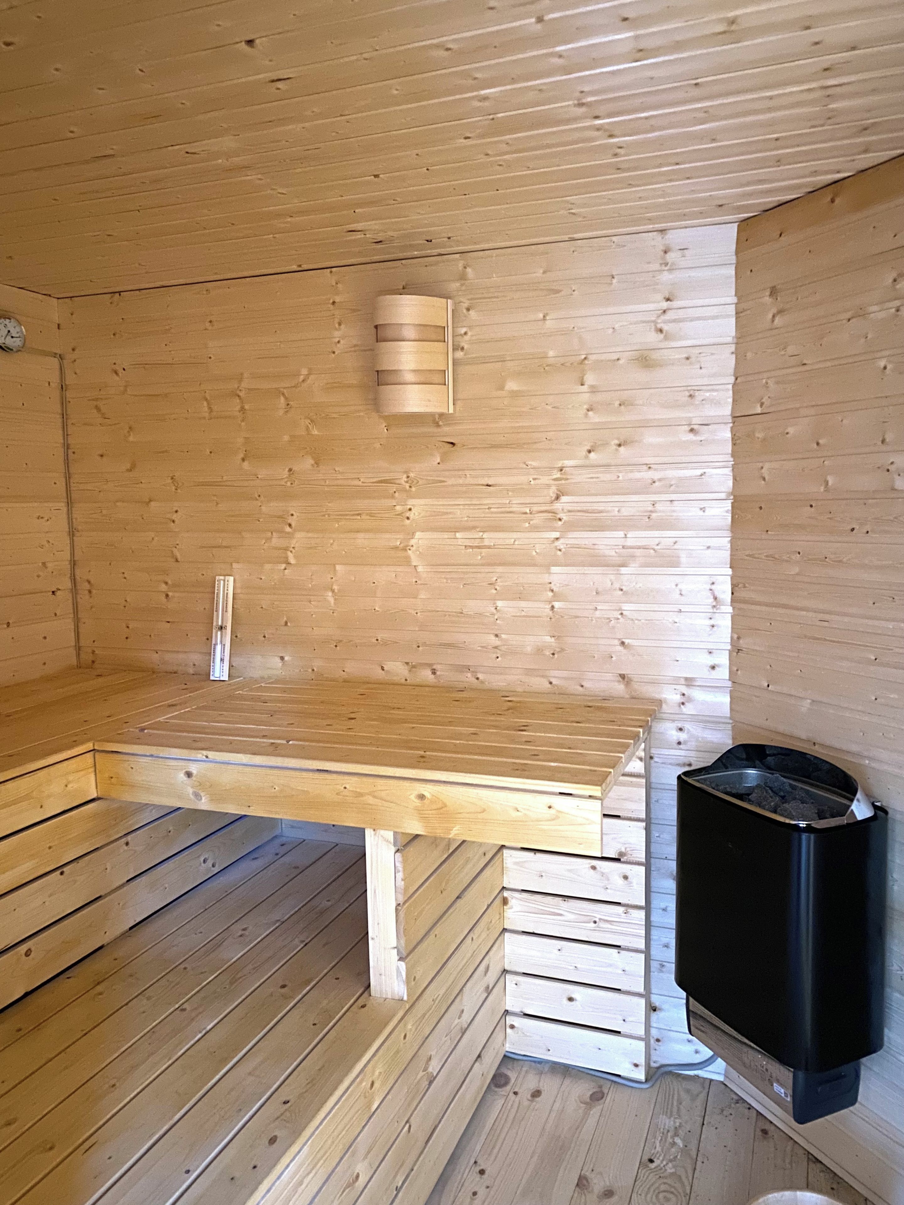 A wooden sauna room with a bench, a wall-mounted heater, and a trash bin.