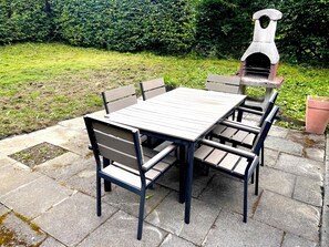 An outdoor patio with a stone table and chairs, a stone pizza oven, and a hedge in the background. - My Time in the Harz Mountains - Your Vacation Home in the Harz Mountains. With a sauna and barbecue area. (Goslar)