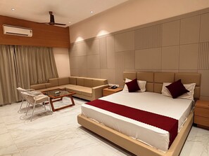 A modern hotel room with a large bed, a sofa, a small table, and a chair. - Raghuvar Hotel and Resto (Ramdevra)