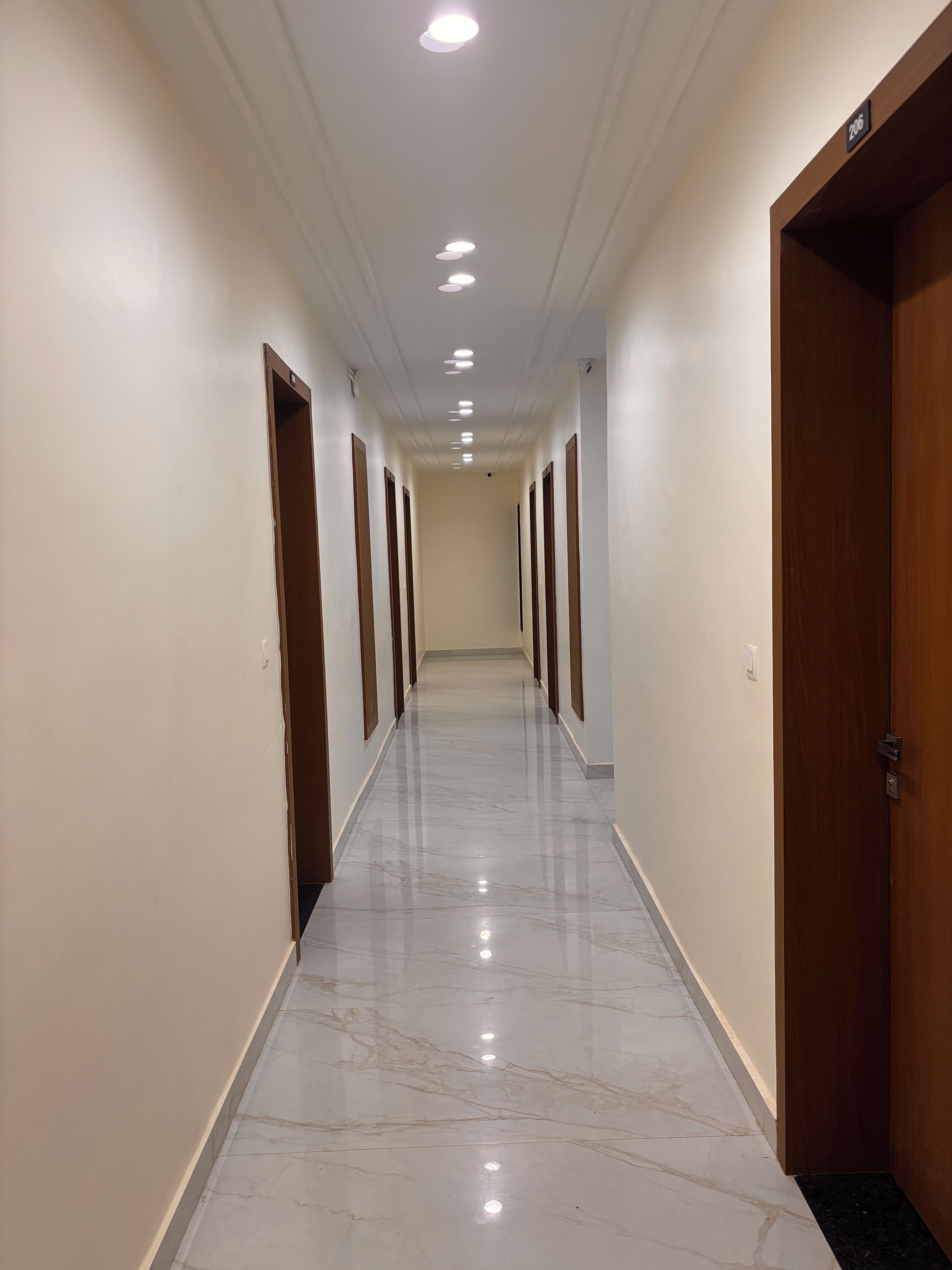 A hallway with a marble floor, wooden doors, and recessed ceiling lights.