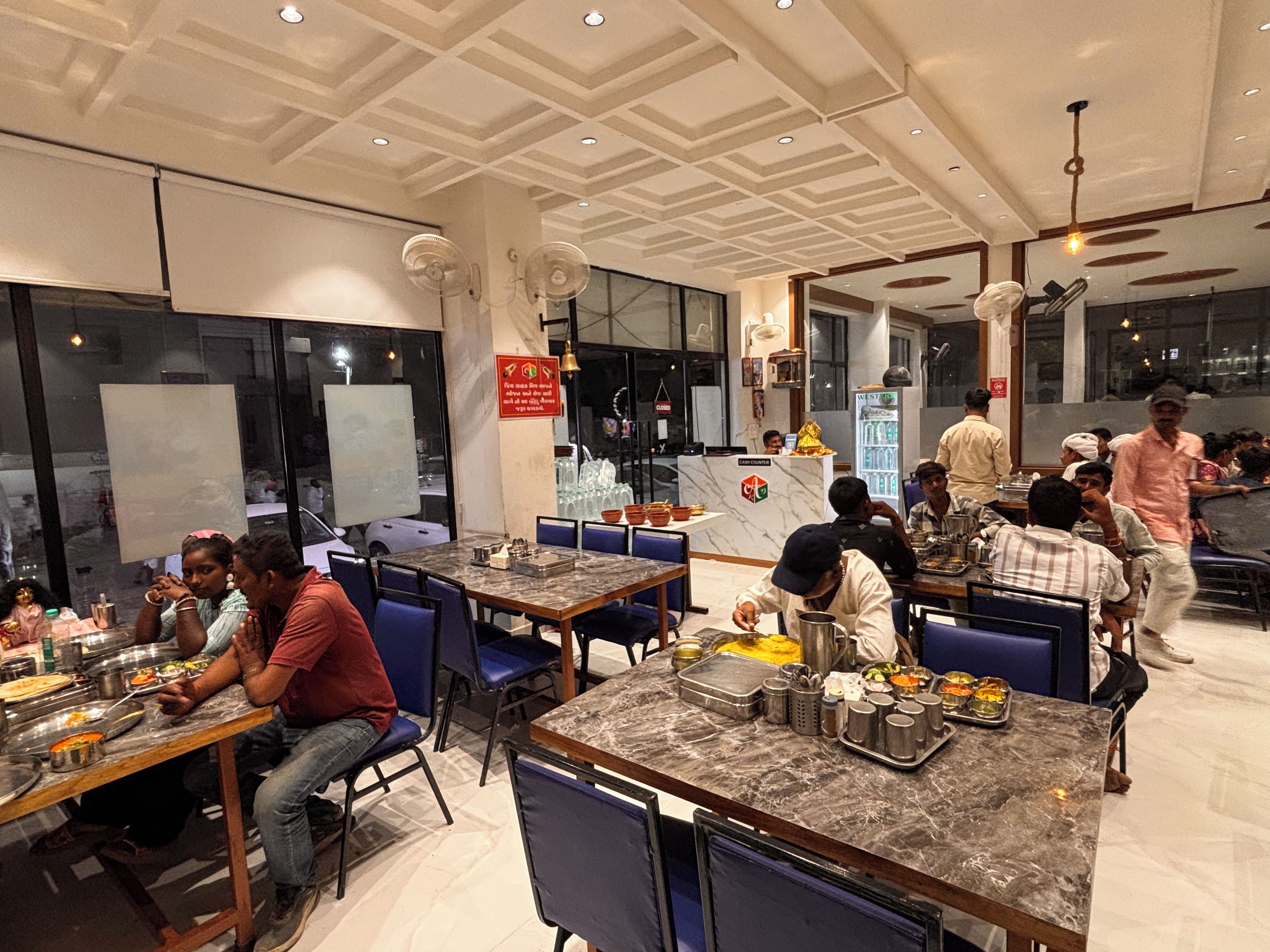 Restaurante com várias mesas e cadeiras, um balcão com registradora e um quadro de cardápio.