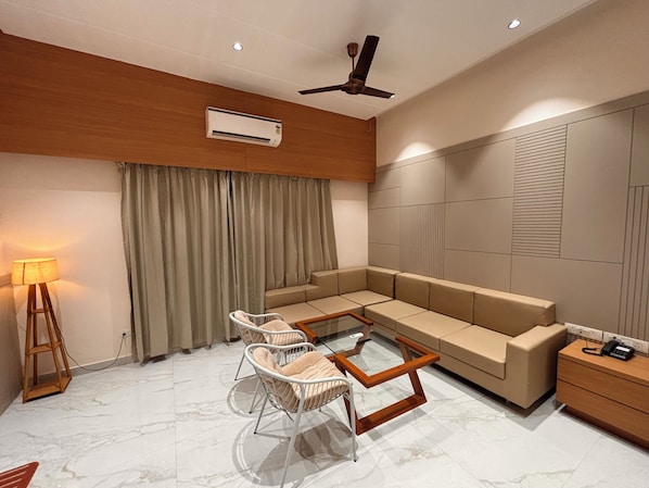 A modern living room with a sofa, two armchairs, a glass coffee table, a standing lamp, an air conditioner, and a ceiling fan.