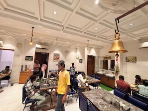 A restaurant with multiple dining tables and chairs, a kitchen area, and a bell on the ceiling.