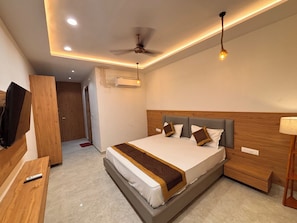 A modern hotel room with a bed, a ceiling fan, an air conditioning unit, and a television on a wooden stand.