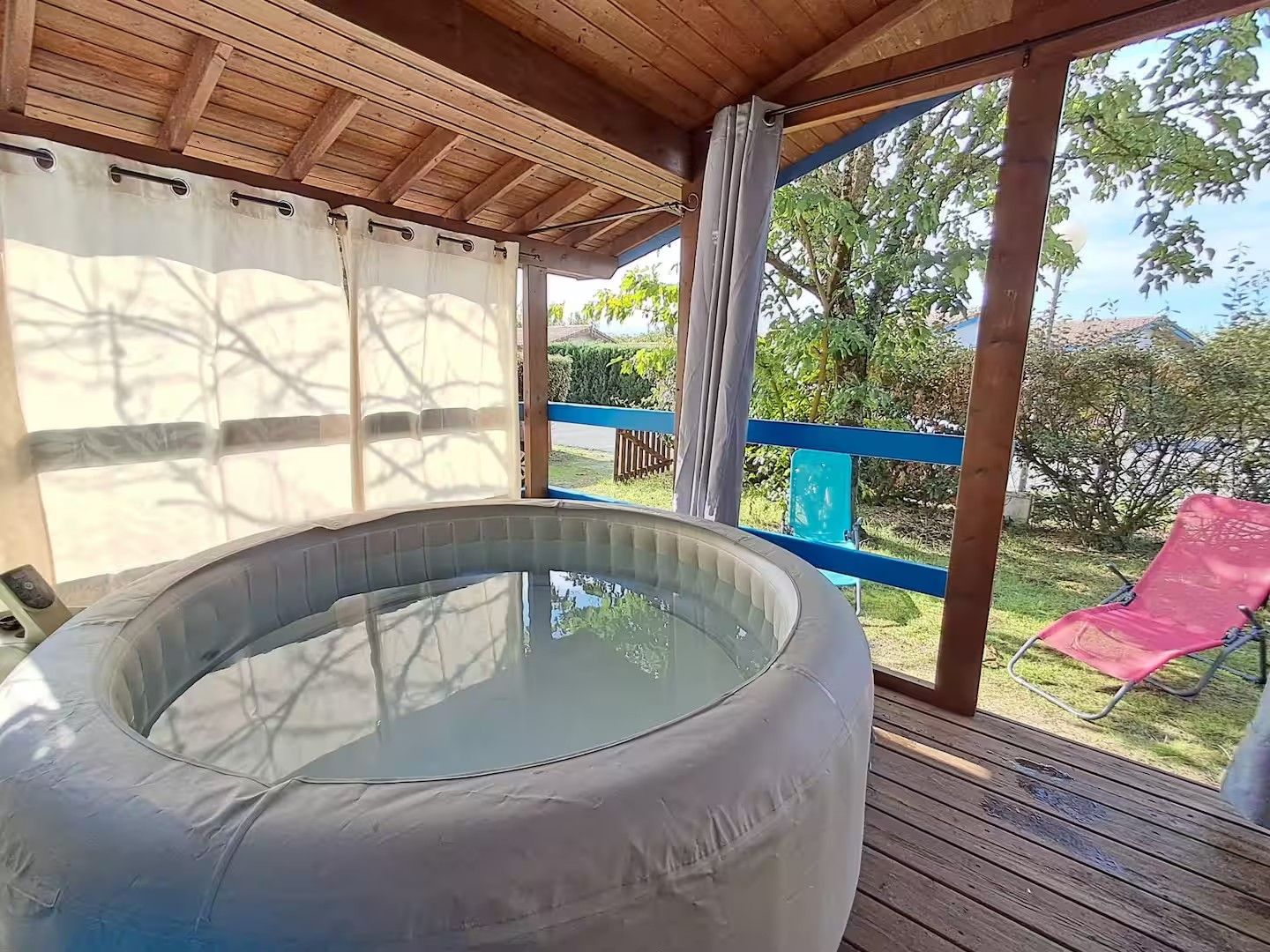 Een hottub op een houten terras met uitzicht op een tuin en een rode stoel.