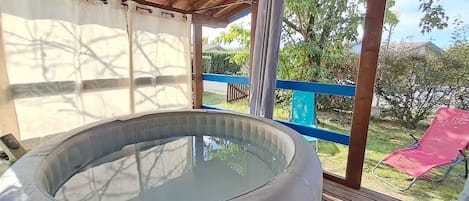 A hot tub on a wooden deck with a view of a garden and a red chair.