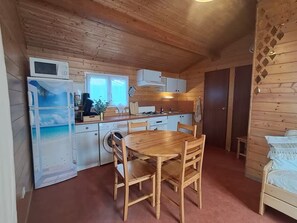 A compact kitchen with wooden walls, a dining table, and basic appliances. - chalet cosy-mer-piscine (Lanton)