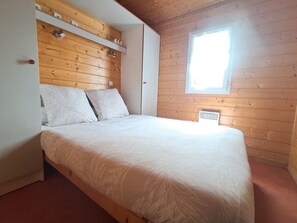 A bedroom with a wooden ceiling, a bed with white bedding, and a window. - chalet cosy-mer-piscine (Lanton)