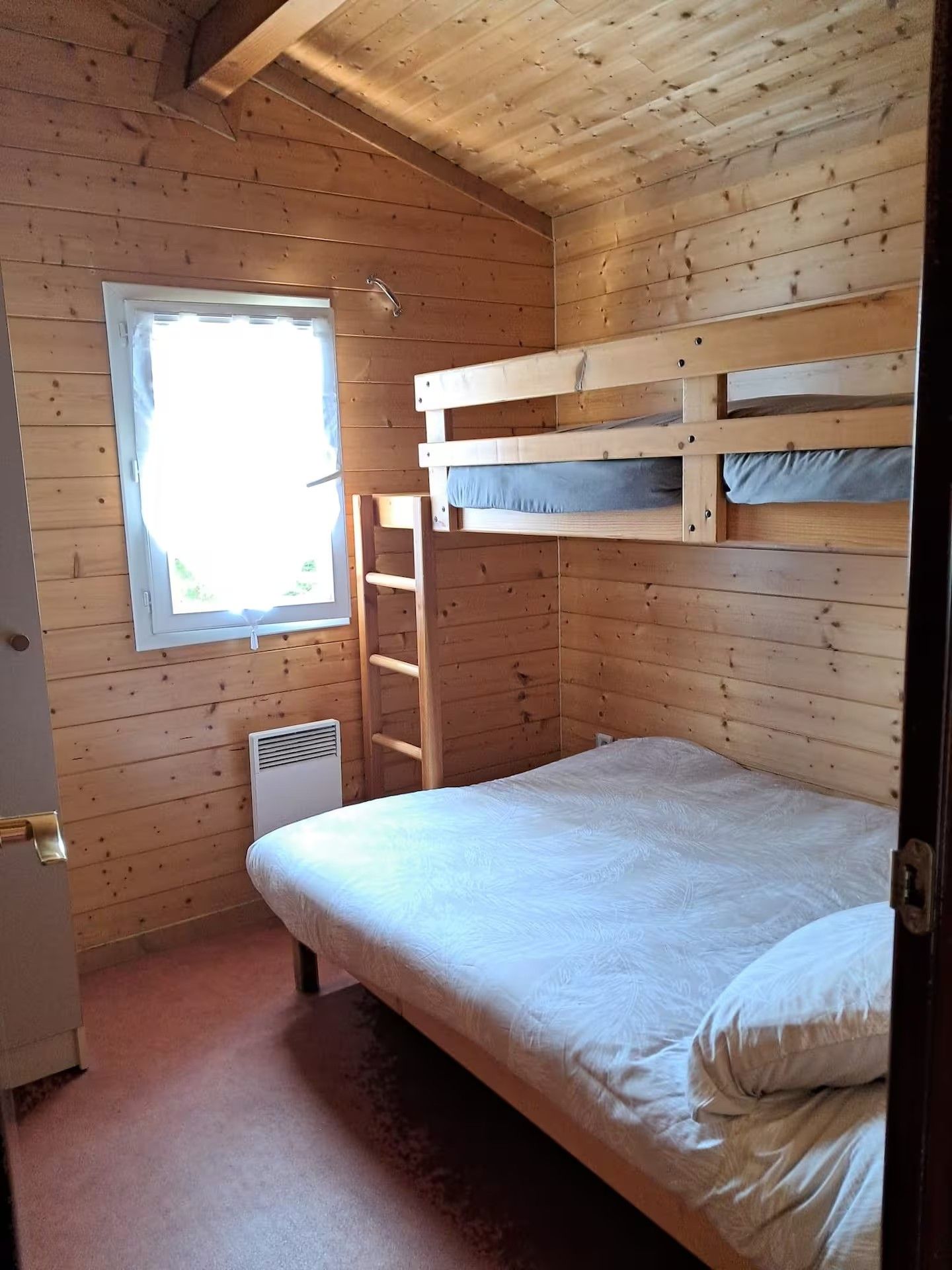 A wooden bunk bed room with a window, a radiator, and a door.