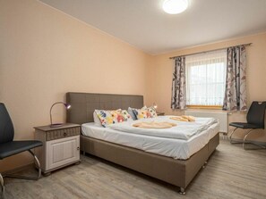 Ein Schlafzimmer mit Bett, Nachttischen, einem Sessel, einem Schreibtisch und einem Fenster mit Vorhängen.