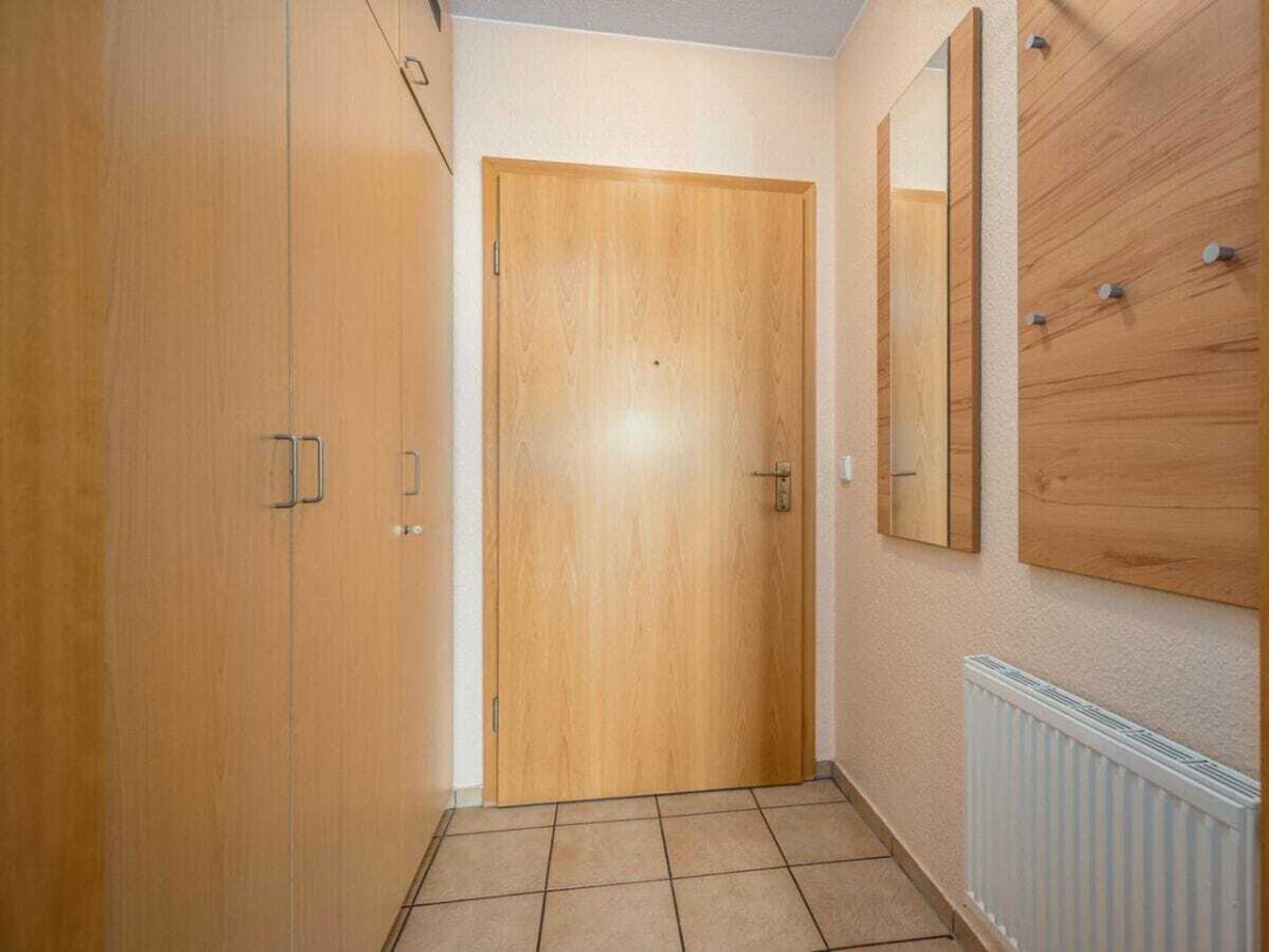 A hallway with a wooden door, a mirror on the wall, and a radiator.