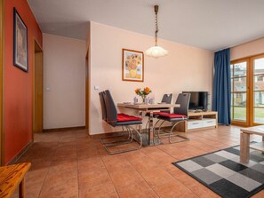 Ein modernes Wohnzimmer mit Essbereich, Fernseher und einem großen Fenster mit Vorhängen.