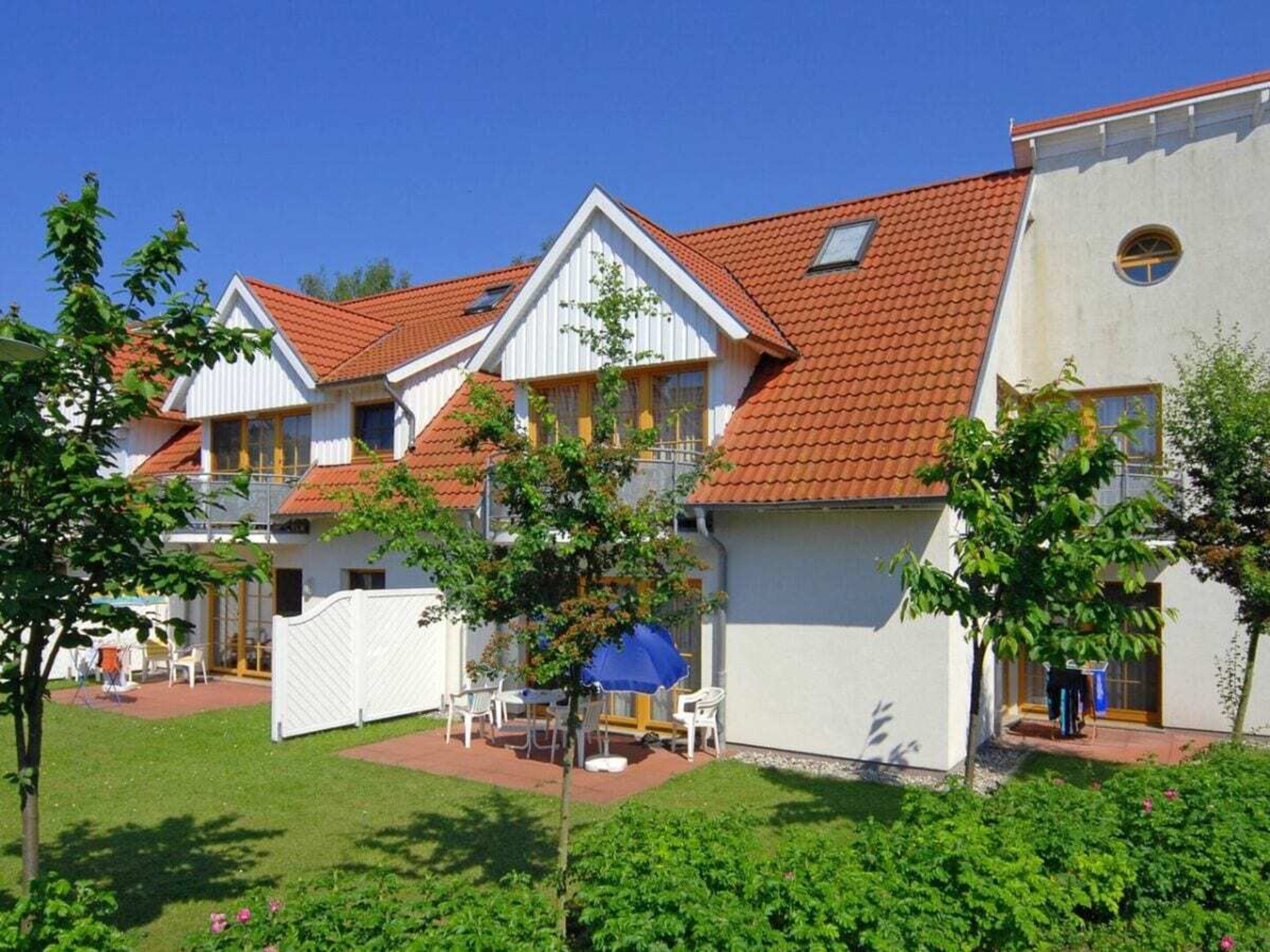 A row of white buildings with red-tiled roofs, a covered outdoor seating area, and a well-maintained lawn.