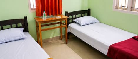 A room with two single beds, a wooden table, a bottle of water, and a red curtain.