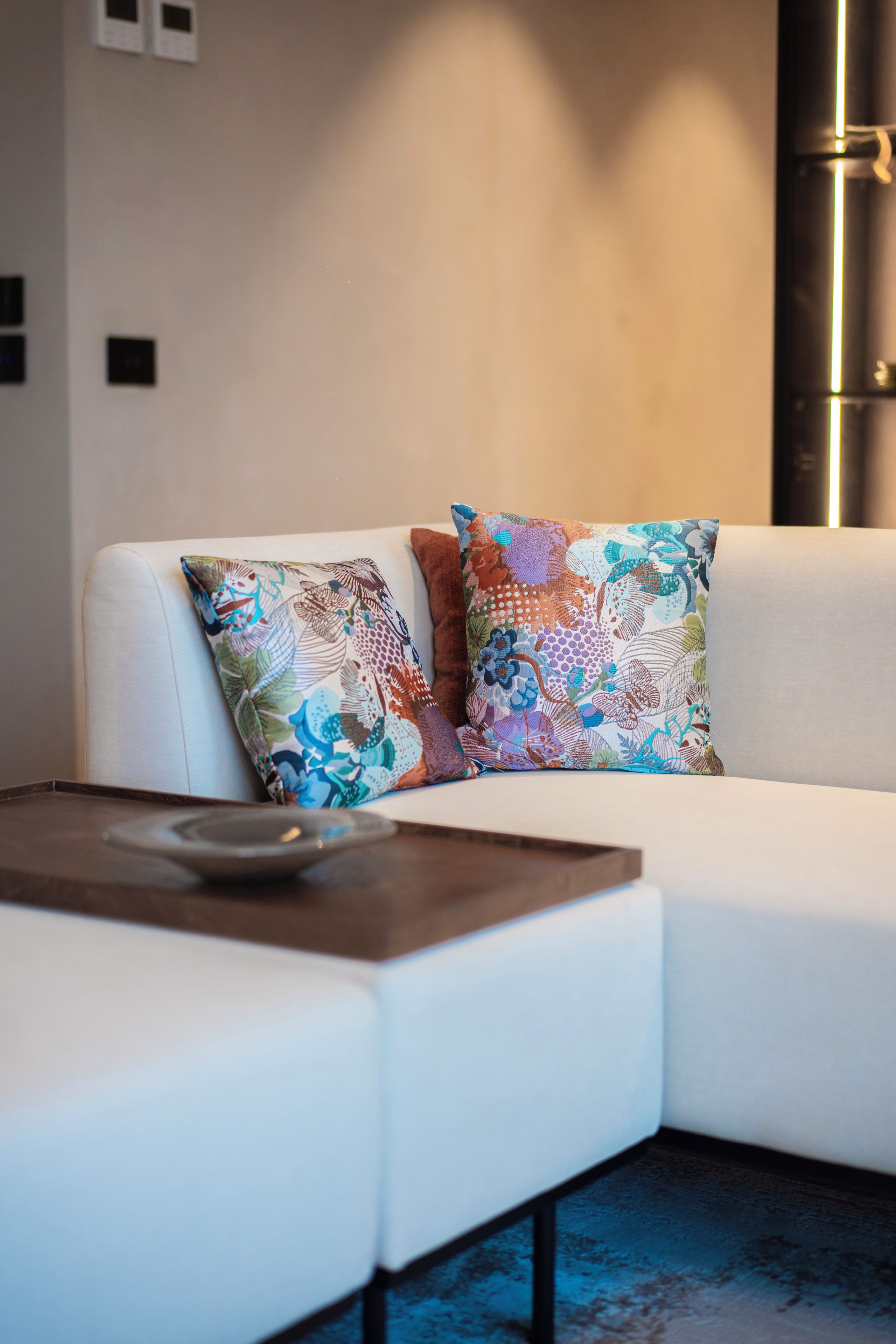 Un salon moderne avec un canapé blanc, deux coussins décoratifs à motifs et une table basse en bois.
