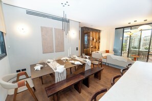 Un comedor moderno con una mesa de madera dispuesta para una comida, un sofá y vistas de la ciudad a través de amplios ventanales.