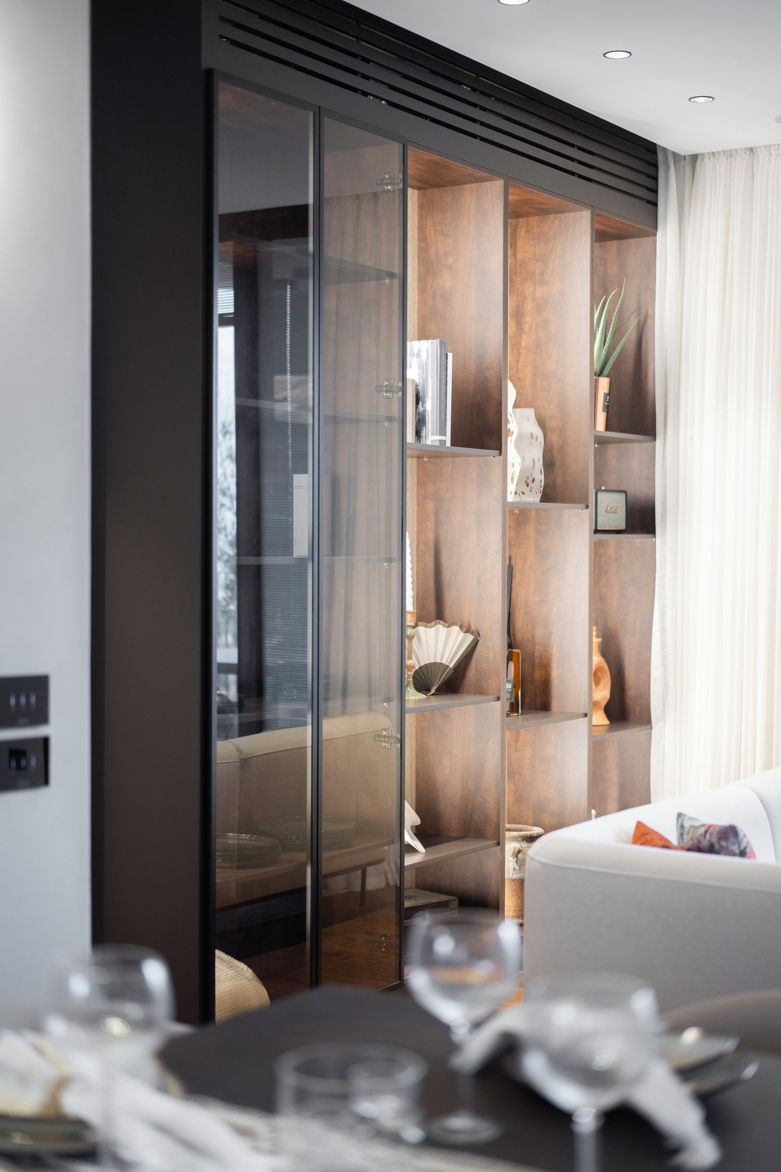 A modern living room with a glass partition, a white sofa, and a dining area with a table set for a meal.
