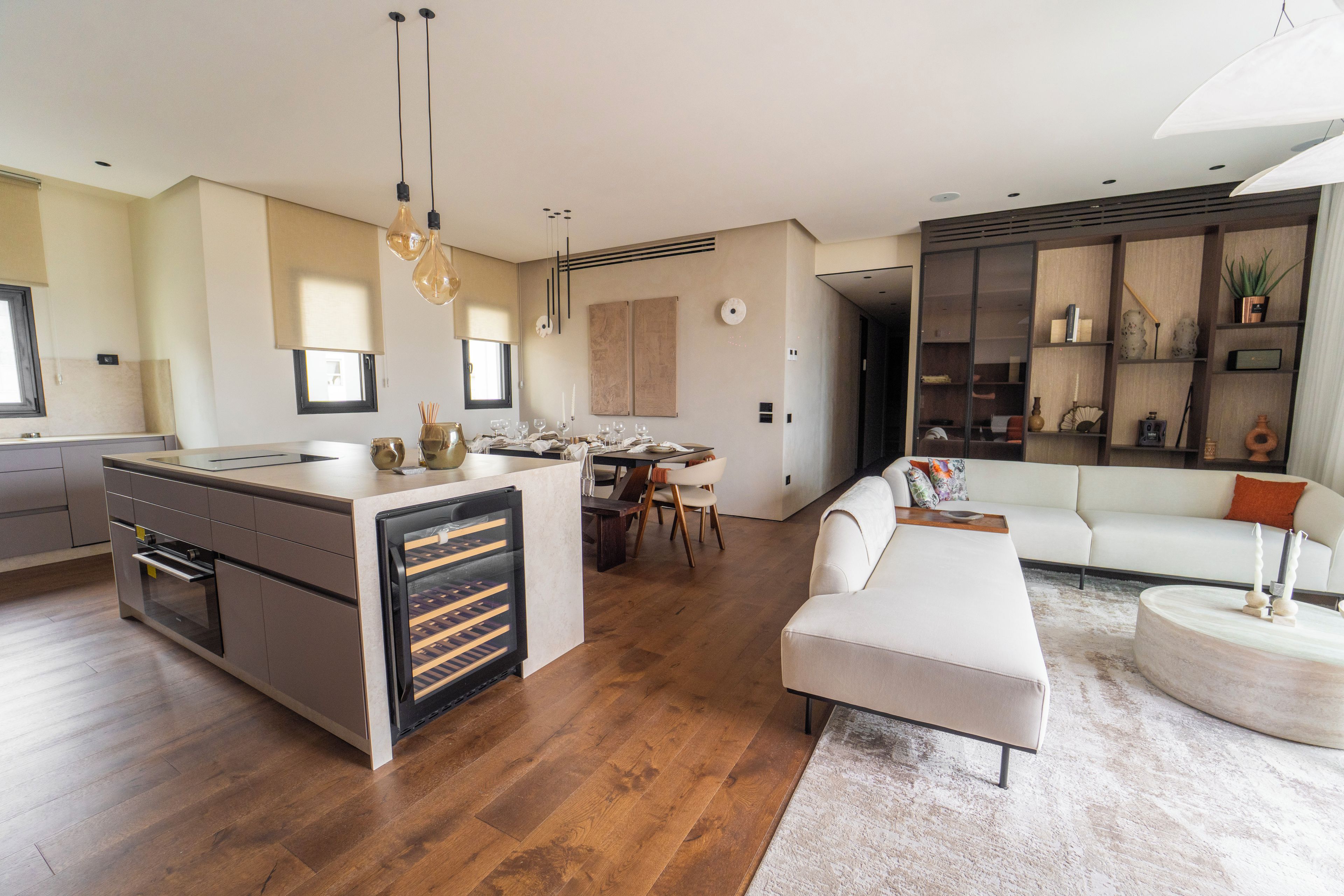 A modern kitchen with a central island, dining area, and a living space with a sofa and coffee table.