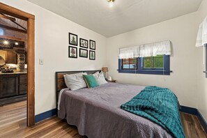 A bedroom with a bed, a nightstand, a window with curtains, and a wall with framed botanical prints. - The Retreat AC+Hot Tub+Pet Friendly (Estes Park)