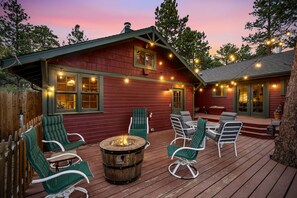 A wooden deck with outdoor seating and a fire pit, surrounded by string lights.