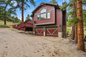 A red two-story house with a covered driveway and a fenced yard. - The Retreat AC+Hot Tub+Pet Friendly (Estes Park)