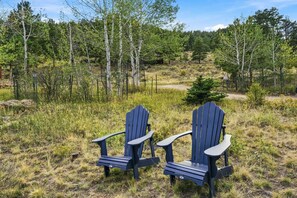 Deux fauteuils Adirondack placés dans un cadre naturel, avec des arbres et de l’herbe.