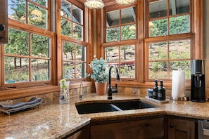 A kitchen with a granite countertop, wooden cabinets, a sink, and large windows with a view of trees.