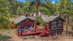 Une cabane à l’extérieur rouge, une terrasse avec des sièges, et un garage visible.