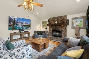 A living room with a stone fireplace, a mounted TV, and a ceiling fan. - The Retreat AC+Hot Tub+Pet Friendly (Estes Park)