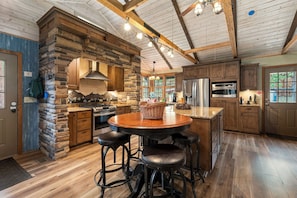A spacious kitchen with a stone accent wall, modern appliances, and a central island with stools. - The Retreat AC+Hot Tub+Pet Friendly (Estes Park)