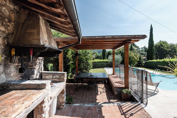 Uma área de pátio com mesa de tijolos, pérgola e piscina.