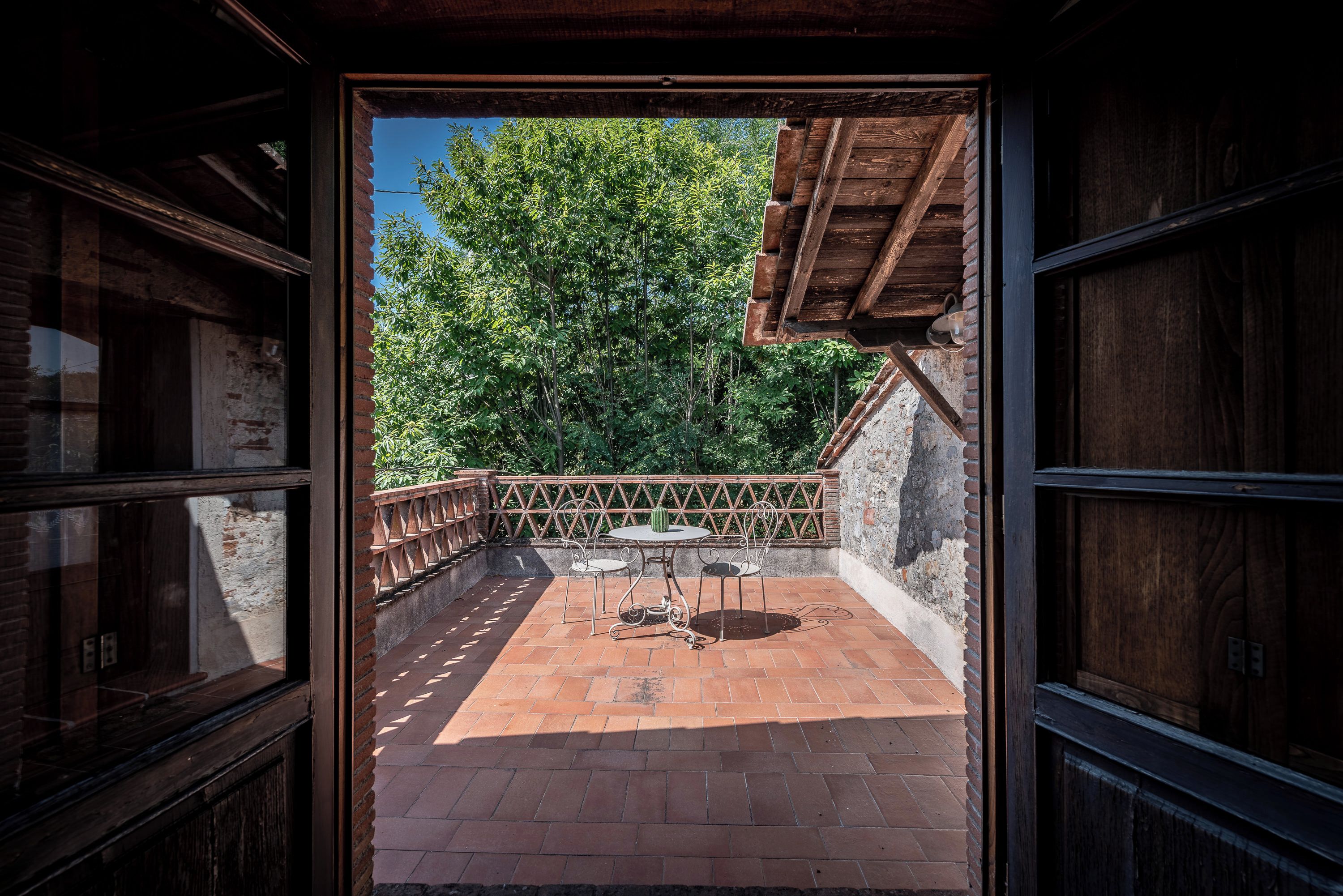 Une terrasse ouverte avec un sol en briques, une table ronde entourée de chaises et une vue sur les arbres.