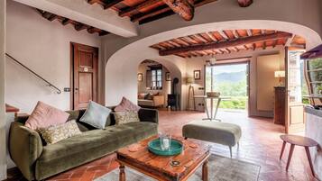 A spacious living area with a green sofa, a wooden coffee table, and a view of a mountainous landscape through an open doorway.