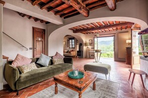 A spacious living area with a green sofa, a wooden coffee table, and a view of a mountainous landscape through an open doorway.