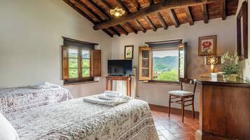 A bedroom with two beds, a TV, and a desk with a chair.