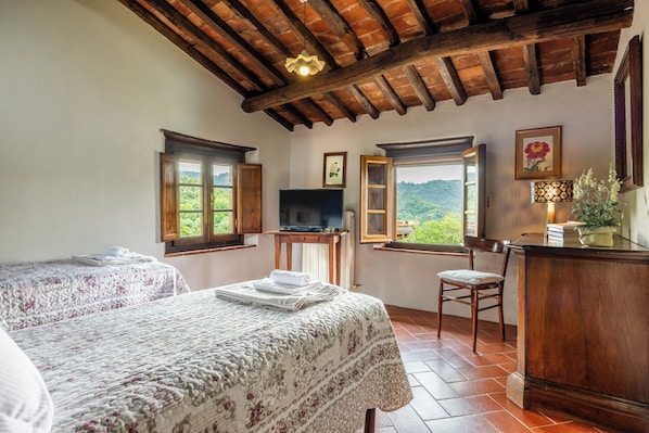 A bedroom with two beds, a TV, and a desk with a chair.