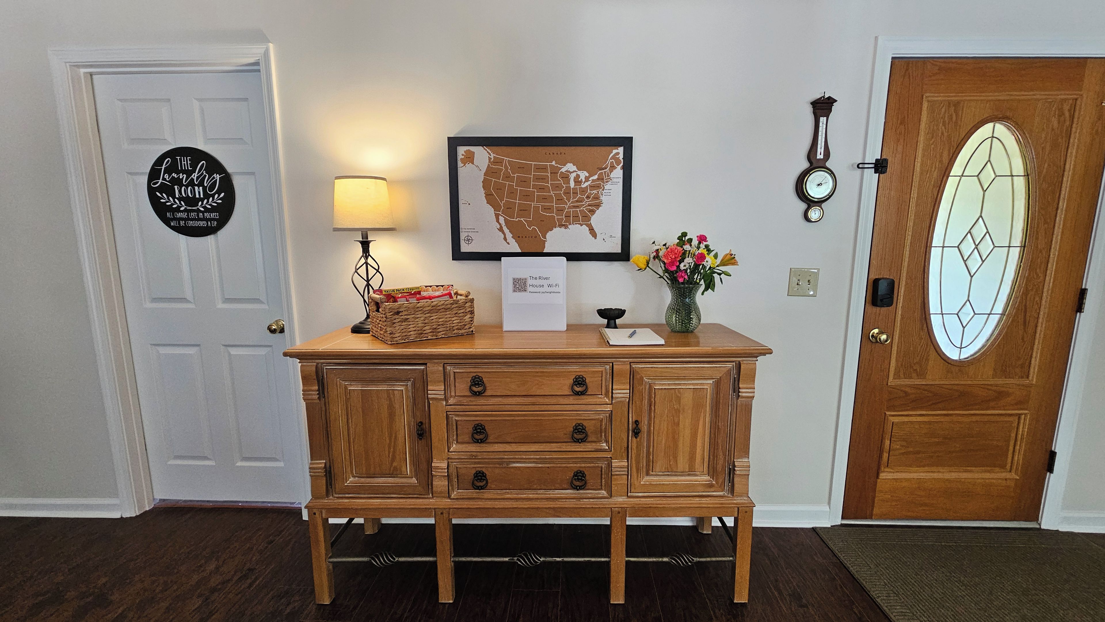 A wooden console table with a lamp, a framed map, and a sign indicating a laundry room.
