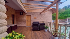 A wooden deck with a glass ceiling, wicker furniture, and potted plants.