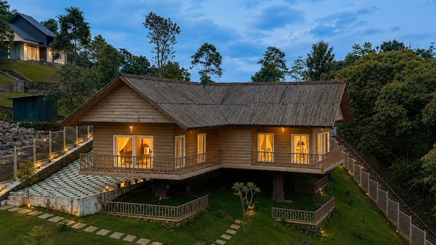 A two-story wooden cabin with a balcony, a stone pathway, and a small garden area.