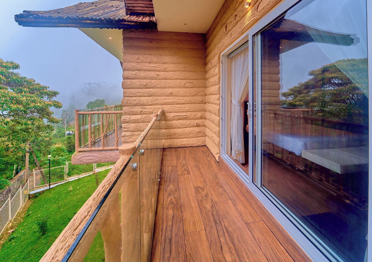 Un balcone in legno con ringhiera in vetro che si affaccia su un paesaggio verde.