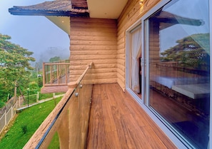 A wooden balcony with a glass railing overlooking a green landscape.