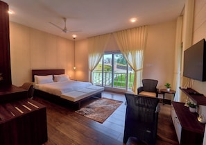 Quarto de hotel com cama, escrivaninha, cadeira, televisão e varanda com cortinas.